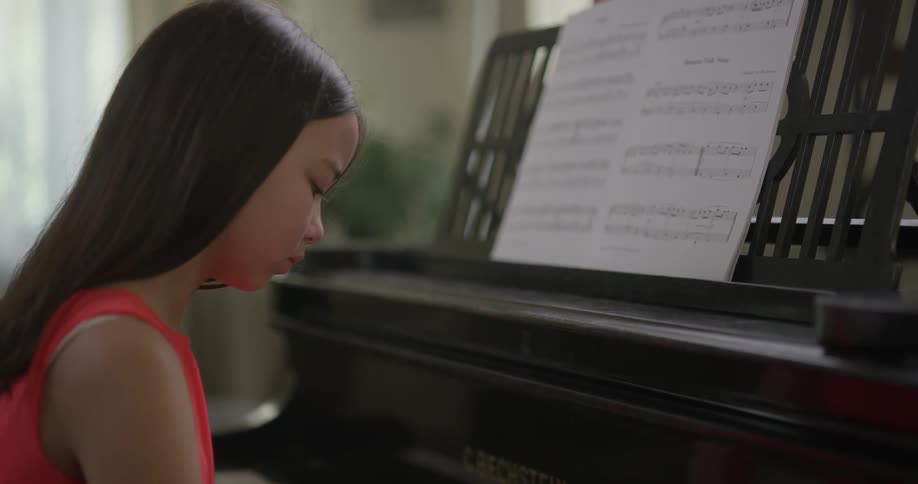 Little girl wearing red dress play the piano indoors during daylight