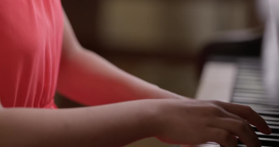 Girl wearing red dress play the piano indoors during daylight