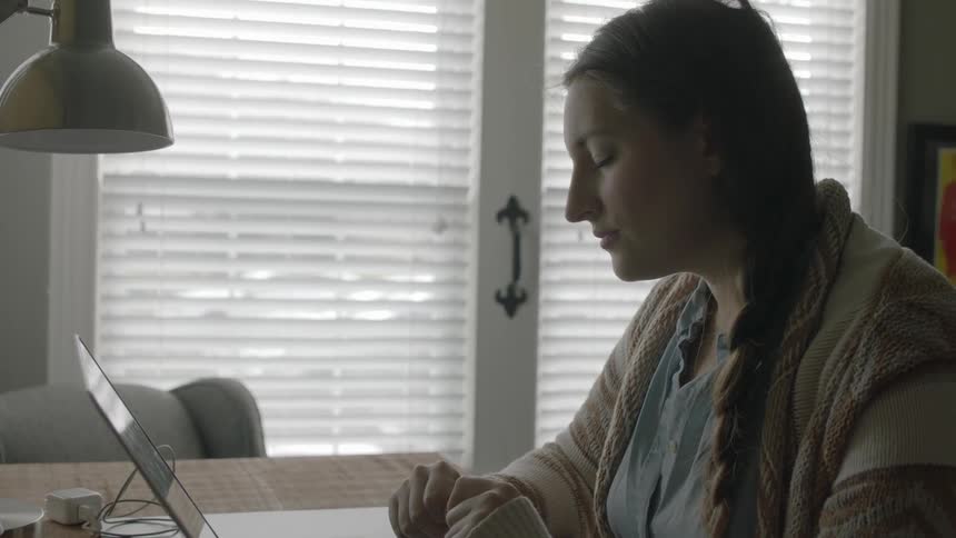 A young woman sits at her desk looking at her laptop screen