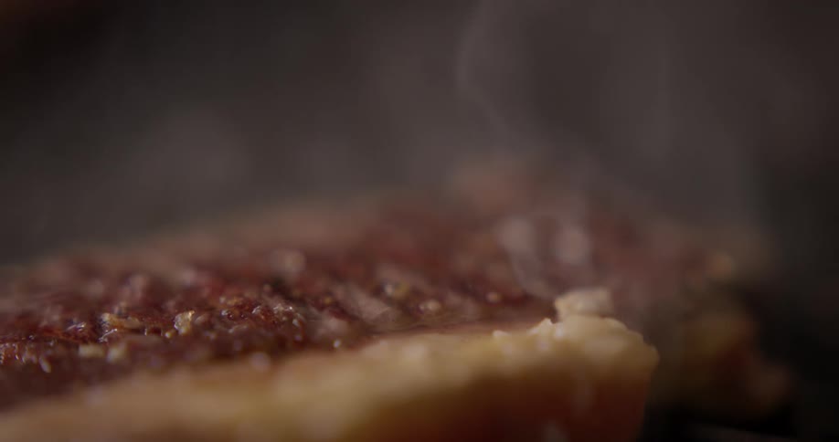 Steam is coming off of a piece of steak that is being cooked on an open grill