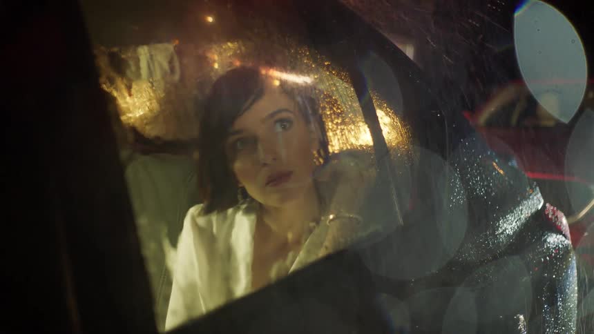 A woman looks out the window of a car into the rain