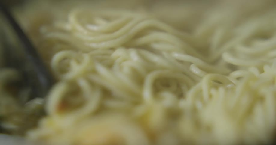 Spaghetti pasta is being stirred indoors during daylight