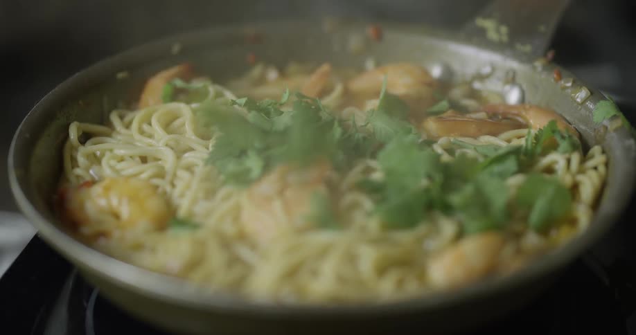 Parsley is being put on the boiling dish in the pan on the stove during daytime