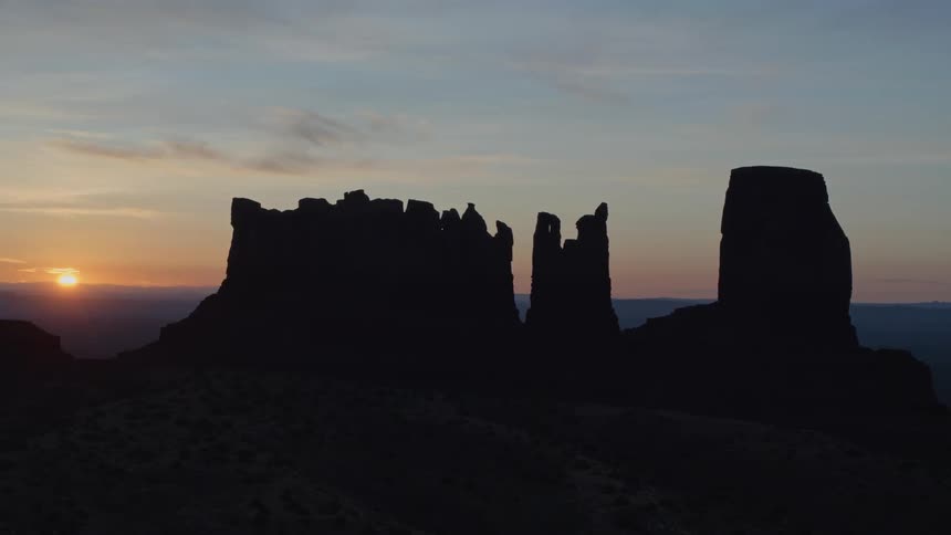 As the sun hangs low in the sky the silhouette of a desert rock formation can be seen towering above the expansive landscape