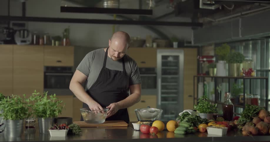 Man in a kitchen washes mushrooms in a glass bowl