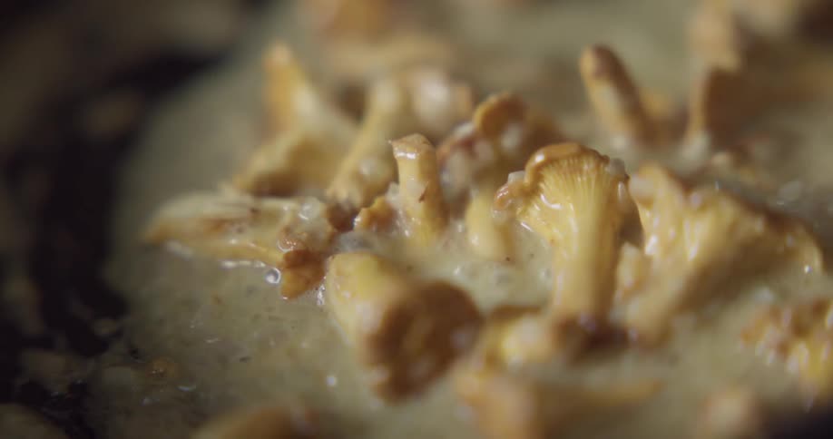 A spoon stirs mushrooms sauteed in butter in a pan