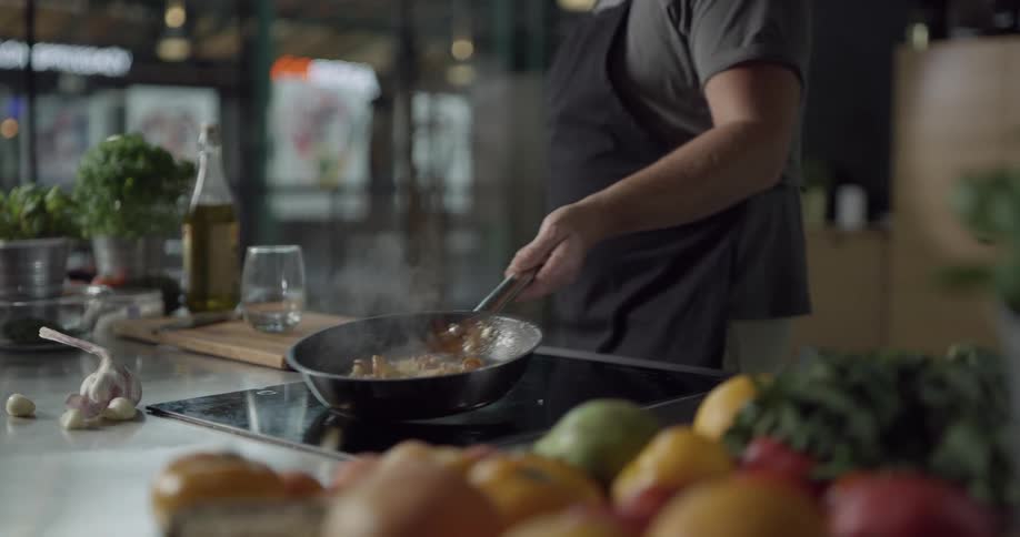 A male chef is moving the steak in a frying pan back and forth on a flat stove top