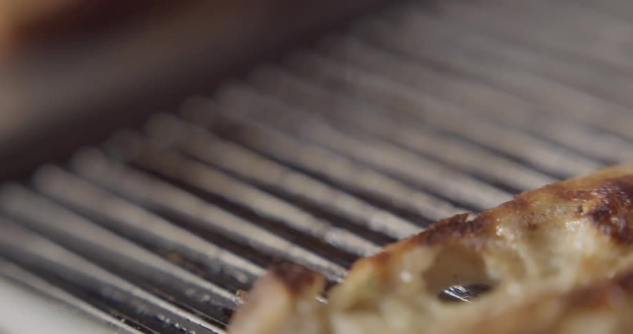 A person picks toast up off a grill
