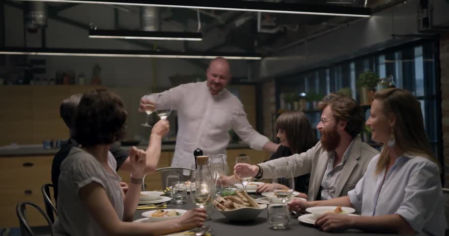 A man serving his friends dinner and toasting with them before sitting down