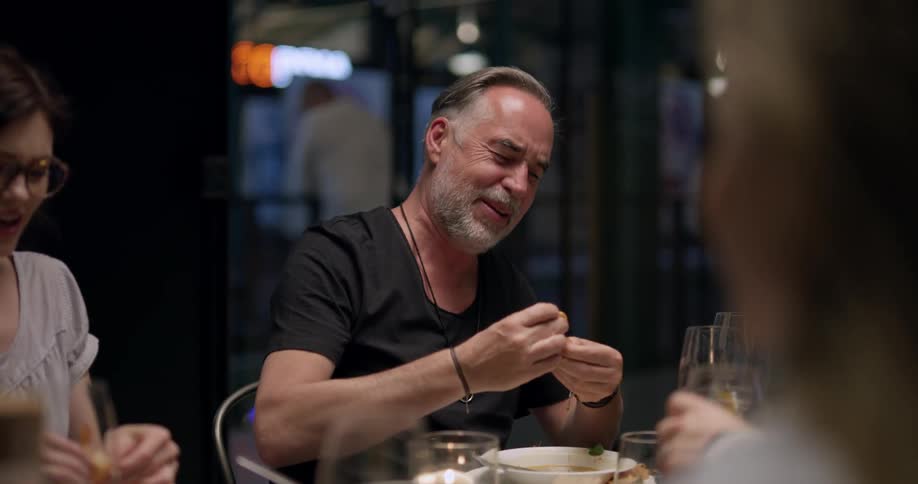 A group of people eat a meal together talking and laughing