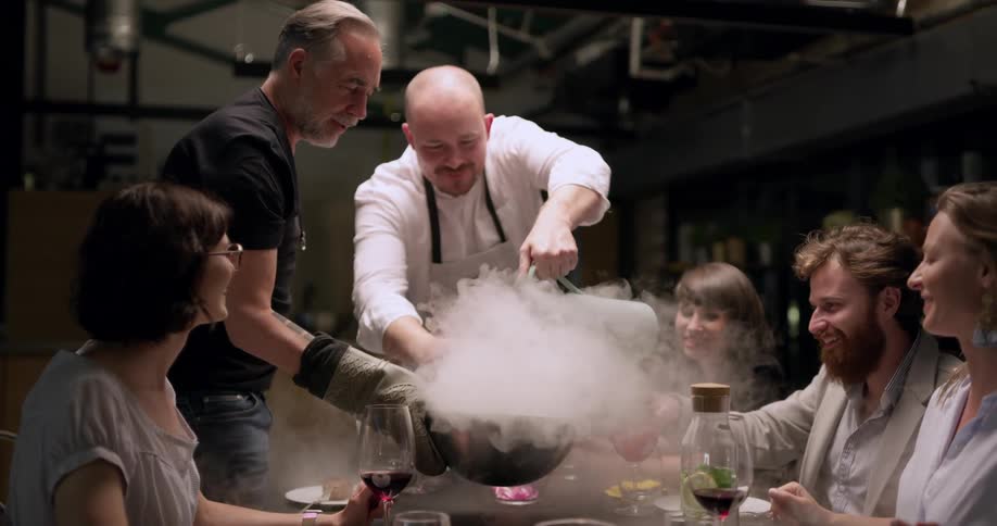 A chef pours liquid nitrogen into a bowl held by a dinner guest at the dinner table