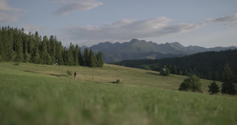 Woman walks on grassland with the view of range of mountains during daylight