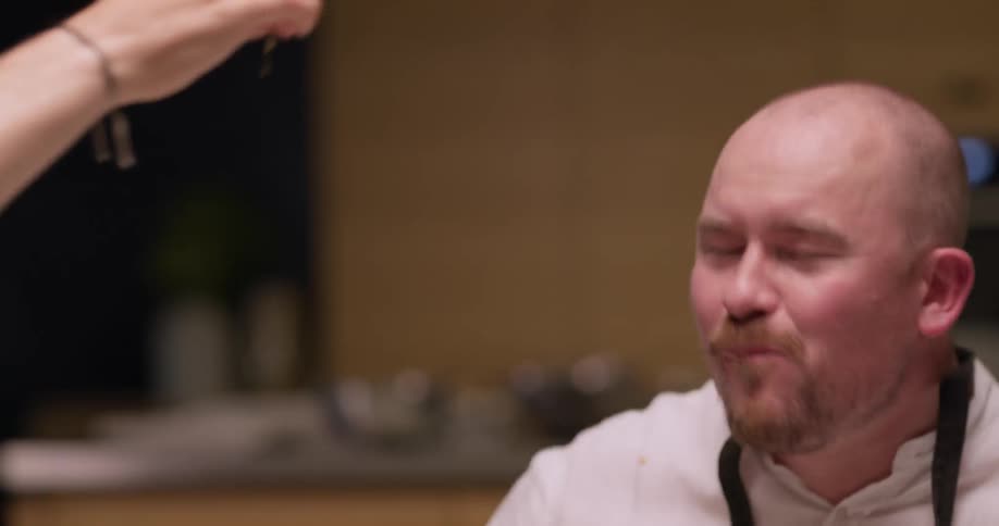 A man sitting at a table feeding a cherry tomato to another man