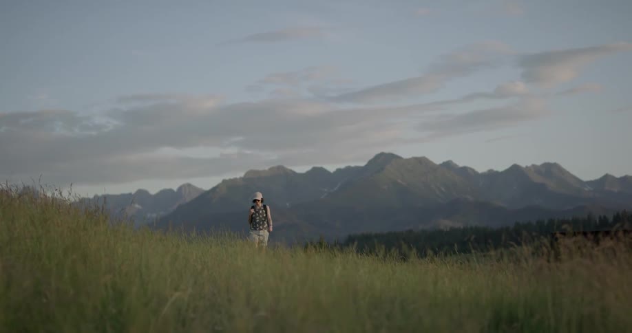 A female hikes through a field with mountains in the distance
