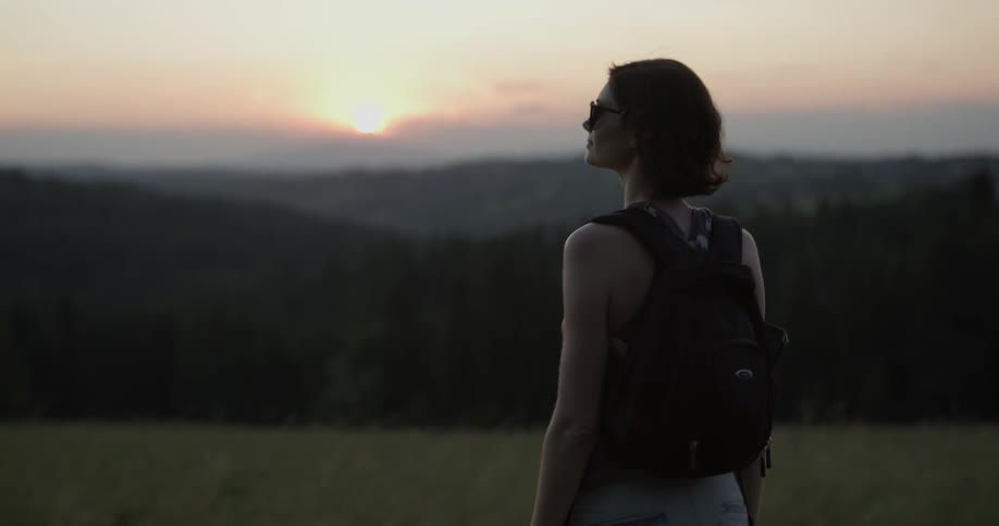 A young woman with a backpack looks across the landscape
