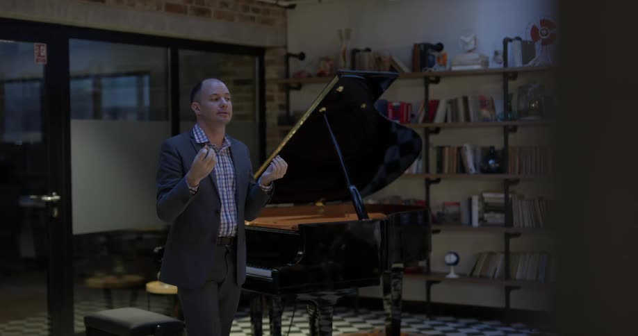 A man stands next to a piano talking