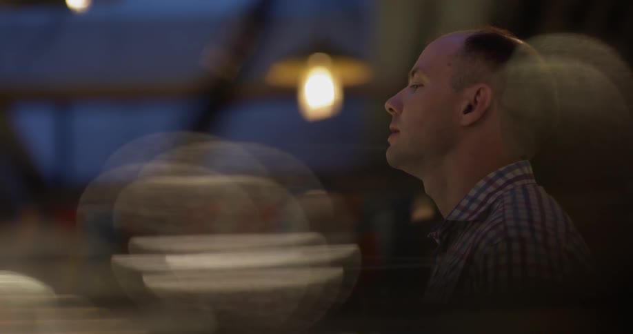 Bald headed man wearing striped shirt talks and holds a bunch of flowers at night