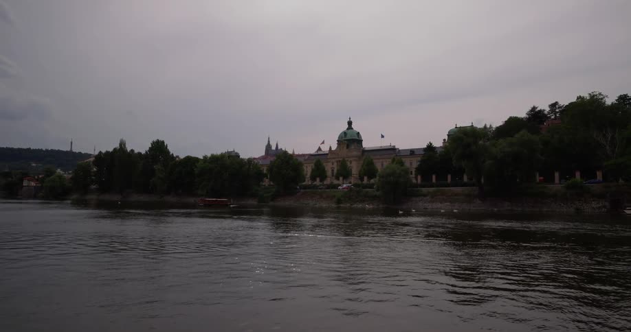 A green domed historic building on the river near a bridge in prague