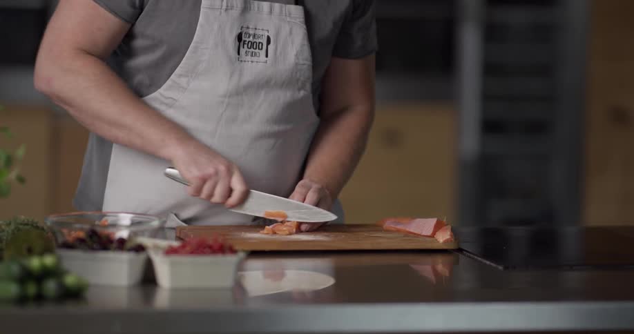 Chef cutting slices of salmon with a knife on a chopping board