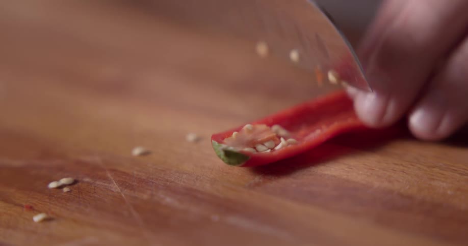 A person scrapes the seeds from a chili pepper using a knife