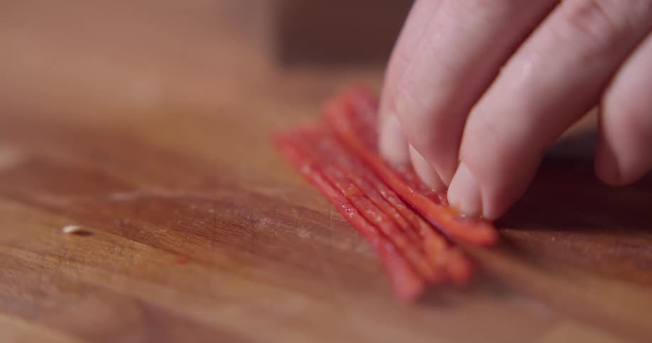 Man cuts half red pepper finely on the cutting board in the kitchen
