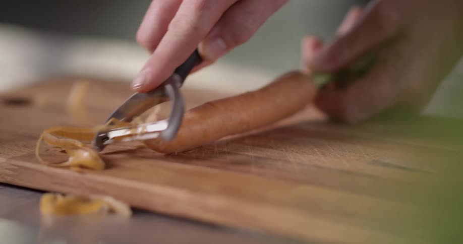 A person shredding the skin off a carrot