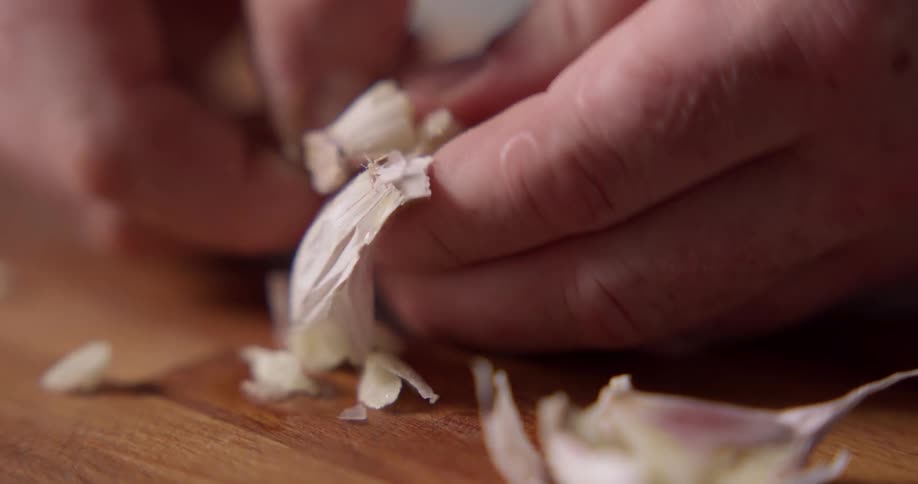 A chef peels garlic cloves on a butcher block cutting board