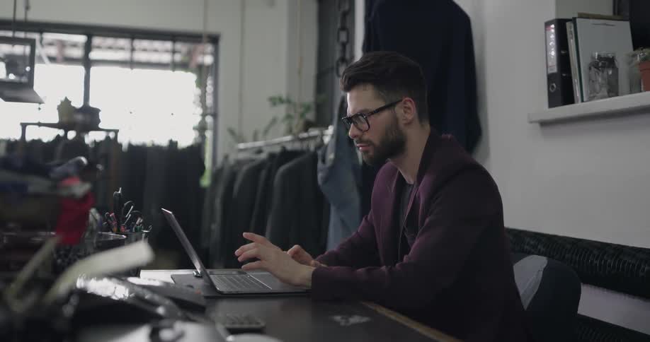 A man is sitting at his desk typing on a laptop