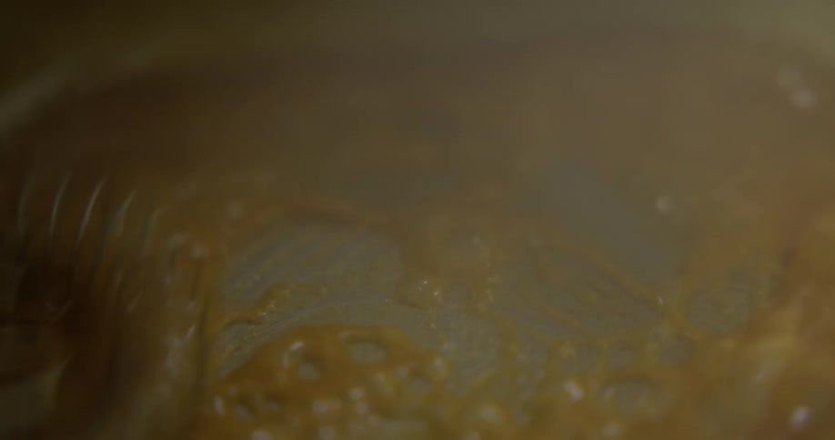 A chef scrapes the bottom of a pan as they stir brown melting butter