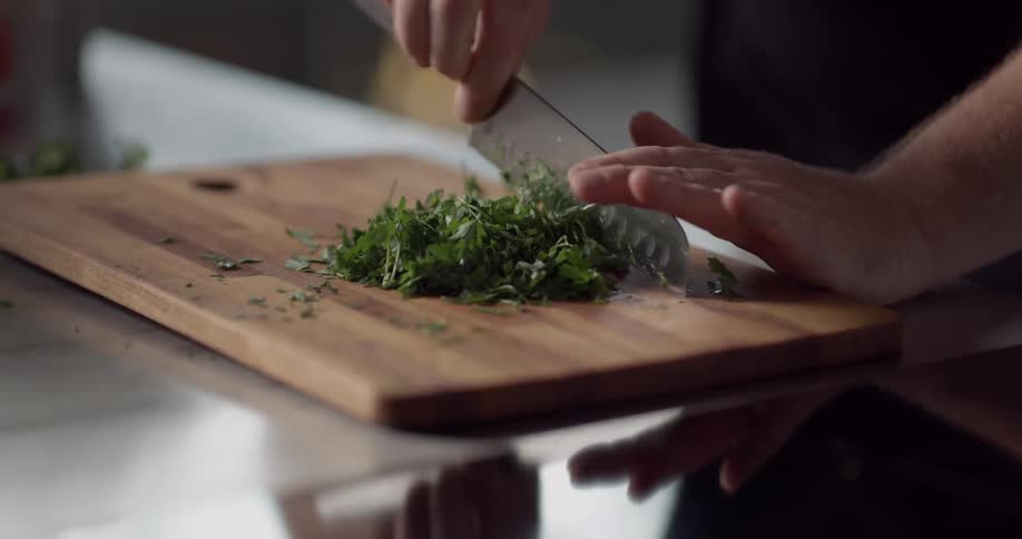 A man chops parsley on a wooden cutting board