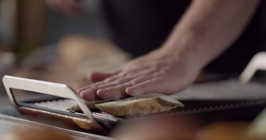 Man toasts slices of bread on grill in the kitchen during daylight