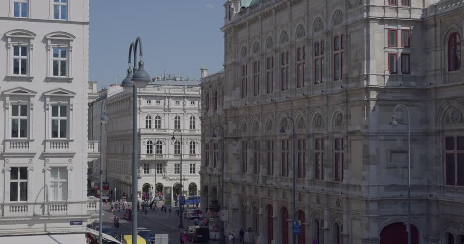 People walk across the street in city with large old buildings on a sunny day