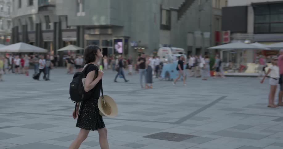 A woman with a black skirt a black blouse and a backpack walking in a city