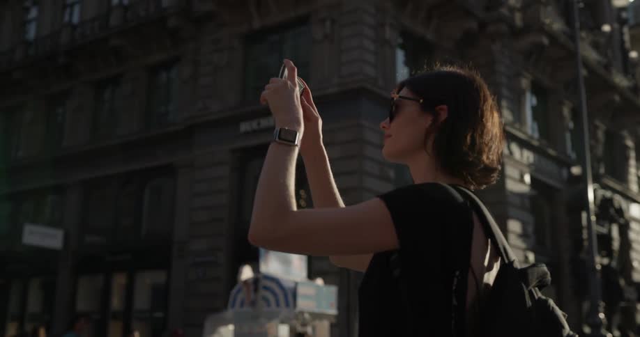 People are walking in the city as a woman takes a photo