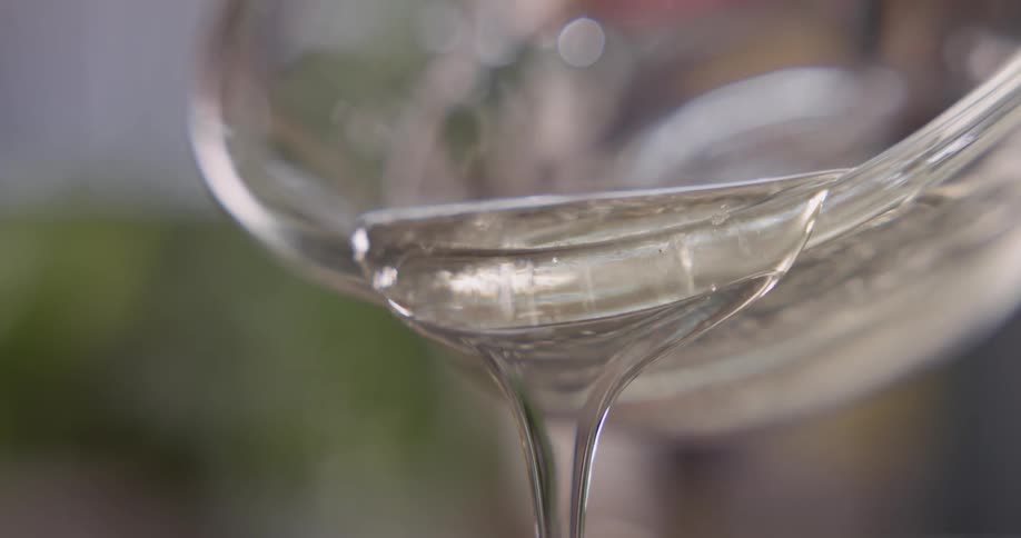 A viscous liquid is poured from a clear glass bowl