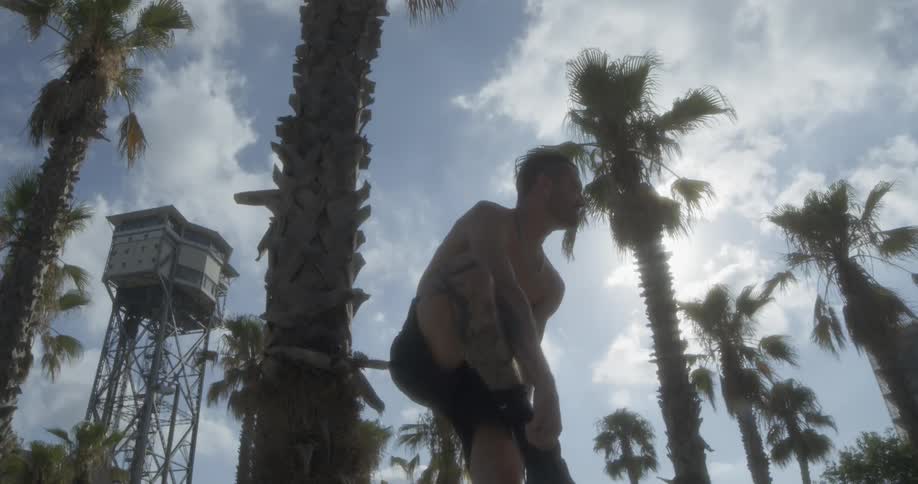 A man puts on a shoe next to a palm tree