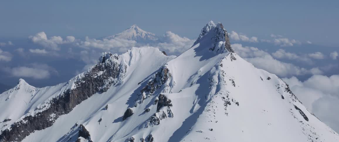 A mountain peak is covered with snow and surrounded by clouds