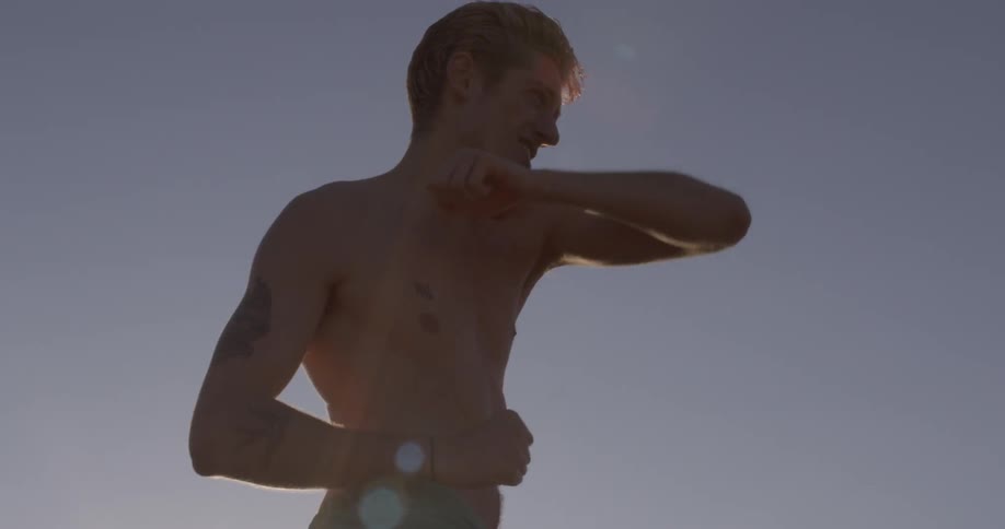 Young caucasian shirtless man is outside practicing fighting moves