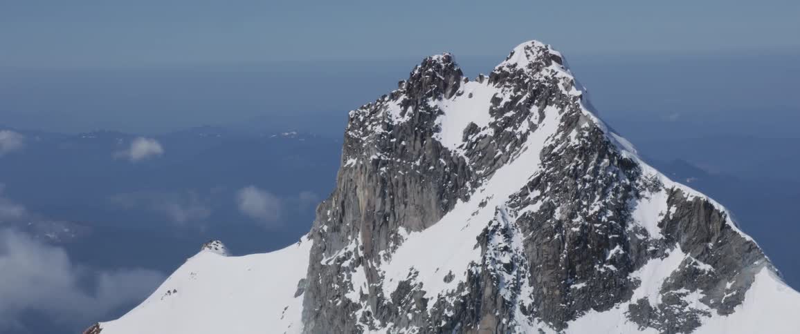 Landscape of the steep snow covered mountain top above clouds during daylight