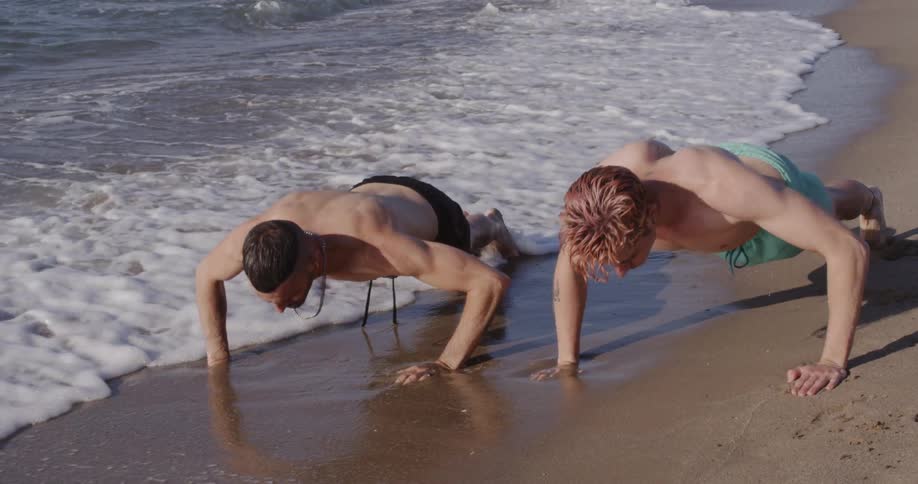 Men doing push ups on the beach next to waves