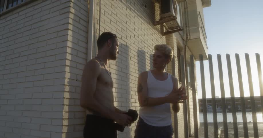 Two men chat outside while standing near a building by a beach