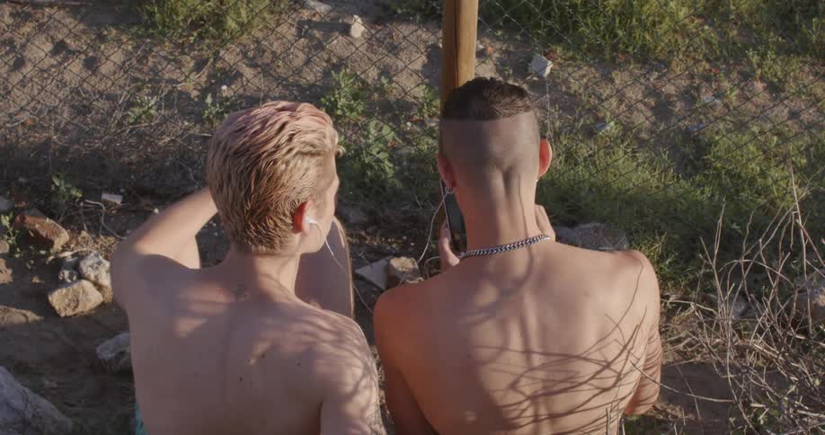Two men sits outdoors sharing music earphones