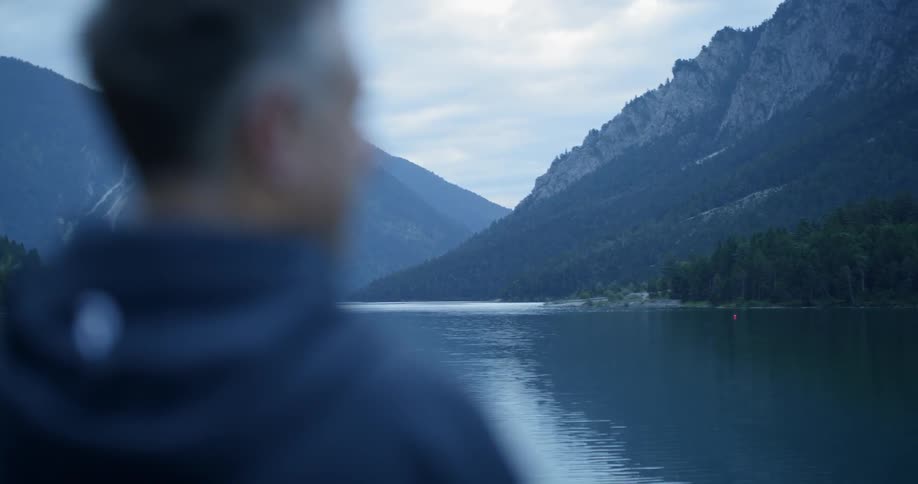 A man looks out to the large mountains and lake
