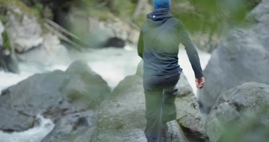 A man climbs up on to large rocks by a river