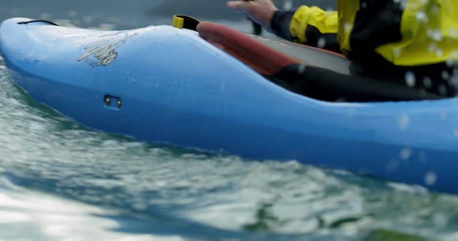 A white man paddles a kayak across a lake