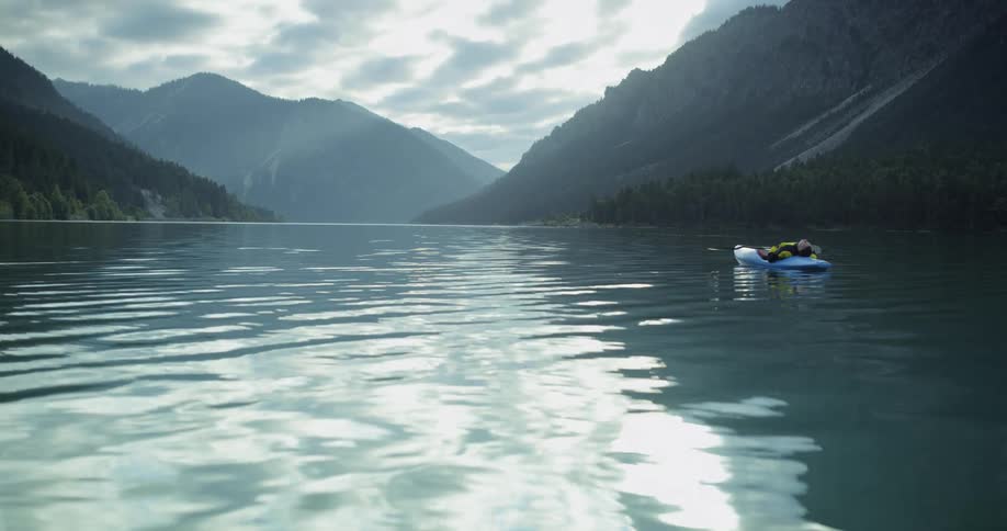 A man in a kayak on a lake surrounded by mountains and forest