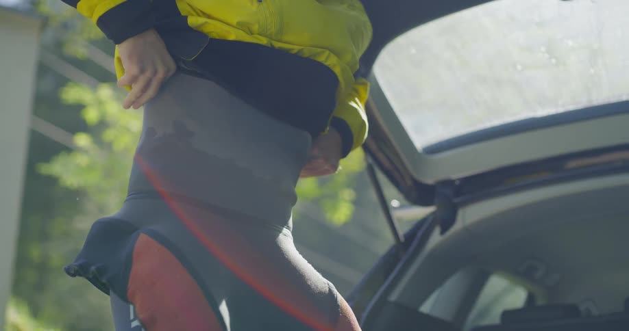 A male standing by a vehicle putting on a wet suit