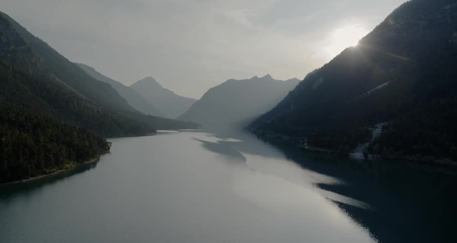 The camera flies over a large lake at the base of mountains