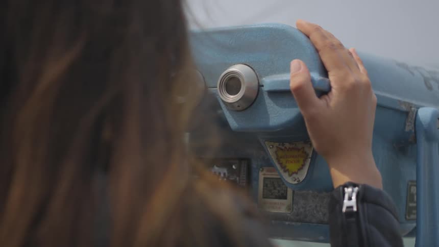 A brunette female looking through a tower viewer towards water