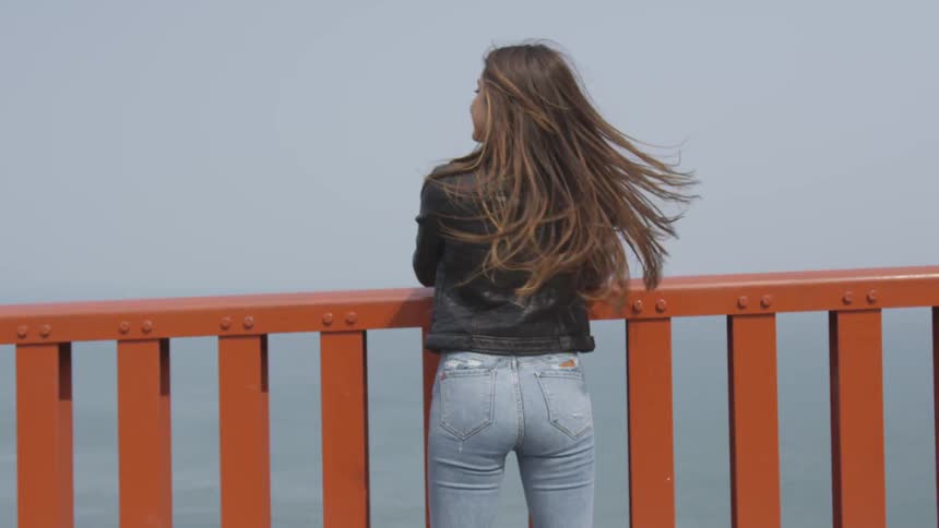 A woman wearing tight jeans leans against railing